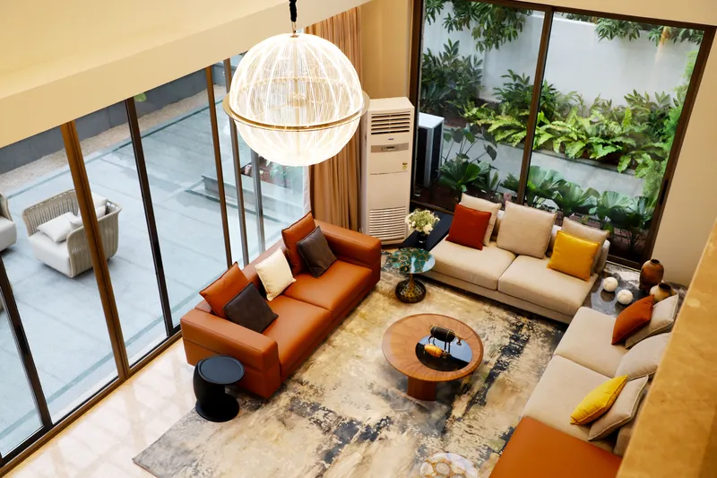 Vista cenital de sala en doble altura con sofá de piel cognac y ventanal completo al jardín